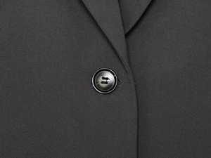 Detail of a black woven blazer featuring a sharp lapel and a single resin button closure