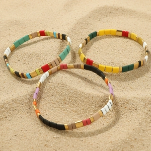 Bohemian colorful painted bead bracelets set of three on sandy beach background