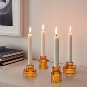 Detailed view of four amber ribbed glass candle holders with lit white taper candles