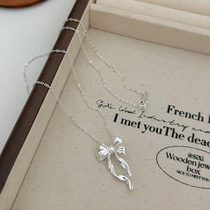 Detail of a 925 sterling silver bow pendant necklace on a wooden jewelry display