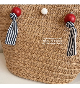 Detailed macro view of straw tote with red beads, blue stripe ribbon, and white pom pom