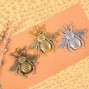Detailed view of three vintage-style bee charms in gold, silver, and bronze metal finishes
