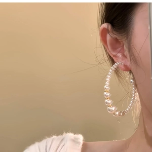 Close-up of elegant gold hoop earrings with beaded pearls worn by a model in soft light
