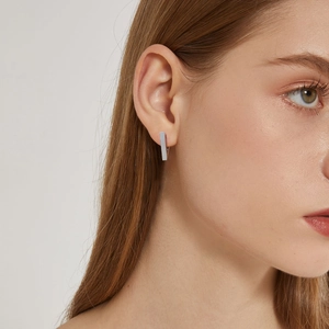 Close-up of a silver rectangular stainless steel huggie earring on a model's ear
