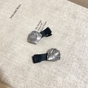 Detailed macro shot of two silver rose petal hair clips with black base on rustic cloth