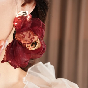 Detail of large wine red chiffon flower earring with polished gold metal on model