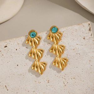 Détail de boucles d'oreilles feuilles dorées avec zircon bleu sur surface en pierre