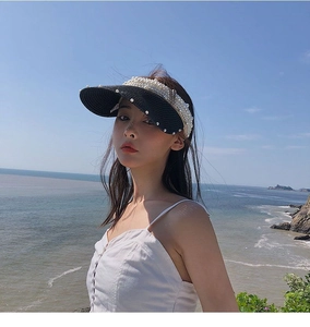 Detail view of black woven straw sun visor with elegant white pearl embellishments