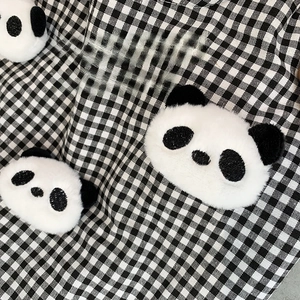 Close-up of 3D plush panda doll attached to a black and white checkered canvas bag fabric
