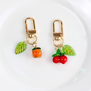 Translucent persimmon and cherry fruit keychains with gold leaves on white plate