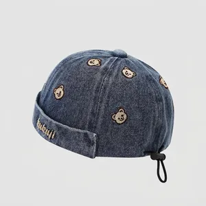 Détail montrant le fermoir réglable et l'ours brodé sur le bonnet en denim
