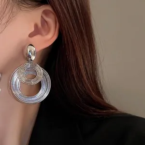 Modern layered silver hoop earrings with a metallic stud on a model in a close-up view