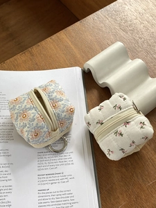 Quilted floral earphone pouches with zipper closure and metal keychain on a book