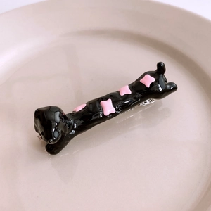 Detail of dachshund hair clip with black resin body and pink bone pattern on ceramic dish