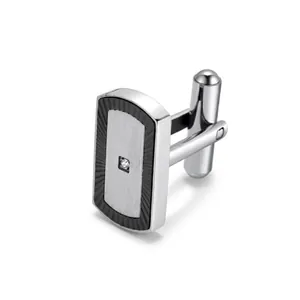 Detail of silver rectangular cufflink featuring brushed metal and a single centered gemstone