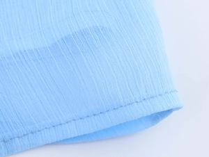 Detailed close-up of light blue chiffon fabric texture and fine stitching on the dress
