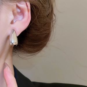 Close-up of polished silver teardrop earrings worn by a model in a minimalist style