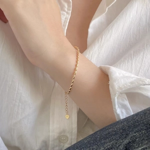 Detail of silver heart charm with S925 hallmark on a dainty beaded gold bracelet