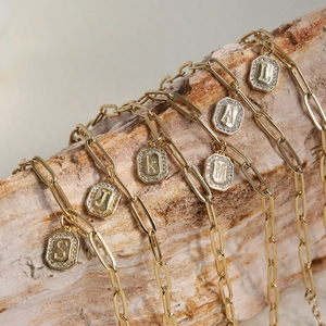 18k gold hexagon initial pendant necklaces on paper clip chains over rustic bark background