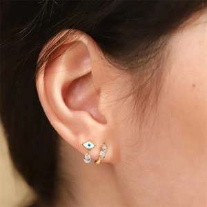 Close-up of gold evil eye drop earring and cubic zirconia hoop on model ear