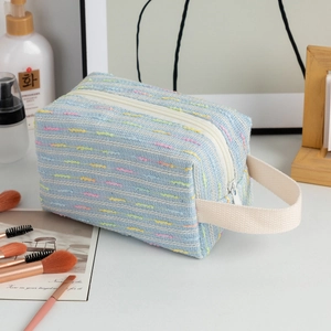 Detail of blue tweed cosmetic bag with white zipper and handle for travel storage