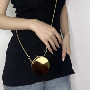 Detail of a mini round gold acrylic evening bag with a slender metallic chain strap