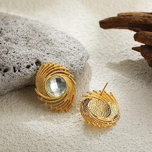 Macro view of gold spiral swirl stud earrings with clear faceted crystal on sand