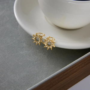 Detail view of gold sun flower ear cuffs with crystals on a white coffee cup saucer