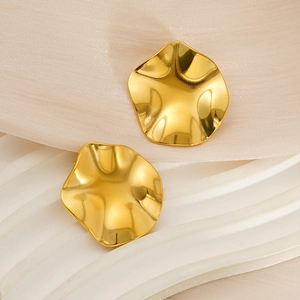 Vue macro détaillée de boucles d'oreilles irrégulières en acier doré sur socle blanc