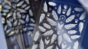 Macro view of crystal 3D nail stickers featuring white wings and crown relief patterns