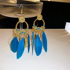 Close-up of bohemian gold earrings with blue feathers and beads on a glass display