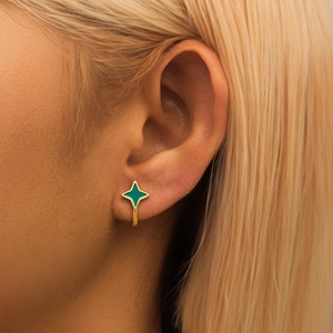 Macro detail of gold four-pointed star earrings with emerald green enamel and crystals
