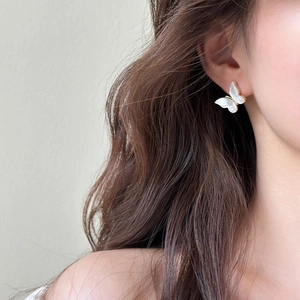 Close-up of a butterfly stud earring with pearl texture and golden edges on a model's ear