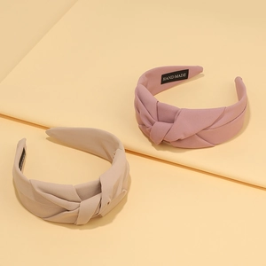 Pink and beige twisted pleated headbands with handmade label on soft fabric background