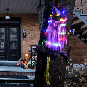Detail of Halloween crashing witch decoration with purple glowing hair and LED lights on tree