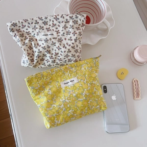 Dettaglio di pochette in cotone floreale con zip ed etichetta simple wish su tavolo