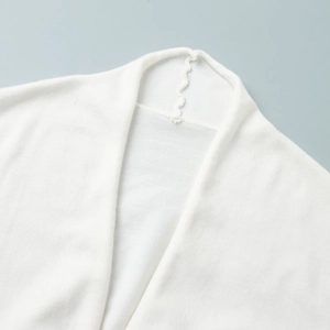 Detail of white knit cardigan neckline showing soft fabric and wave stitching texture
