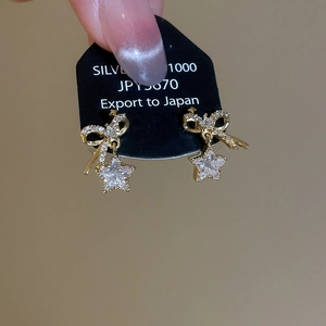 Detailed close-up of gold-plated silver earrings featuring a bow and star zircon pendant