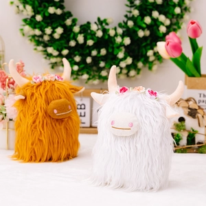 Brown and white highland cow plush toys with floral crowns in a cozy scenic setting