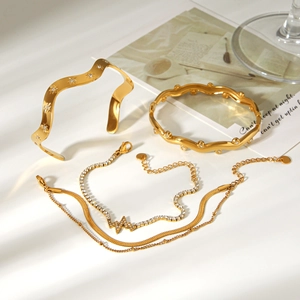 Close-up of golden wave-shaped bangles and rhinestone chain bracelet set on minimalist desk
