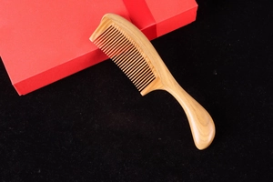 Sandalwood hair comb with round handle and red gift box on a black background