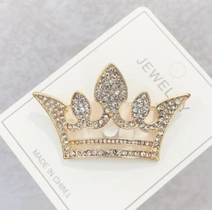 Macro view of gold-plated crown brooch with shimmering white rhinestones on jewelry card