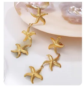 Macro shot of gold-plated starfish drop earrings against a decorative pearl shell