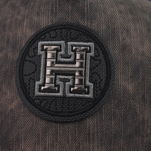 Detailed view of plaid baseball cap featuring a premium metallic H logo emblem