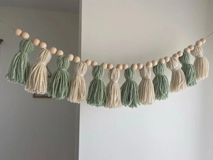 Detail of handmade boho tassel banner with green and beige yarn and natural wooden beads