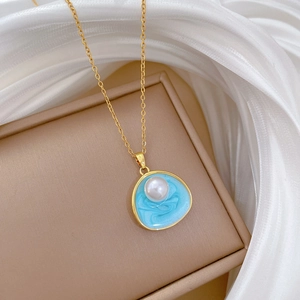 Détail d'un collier doré avec pendentif en résine bleu clair et perle blanche