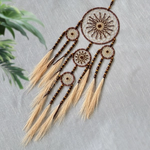 Handmade dream catcher with brown wooden beads and beige feather tassels on gray background