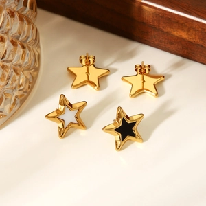 Golden star-shaped earrings with white and black enamel inlay on a wooden tray