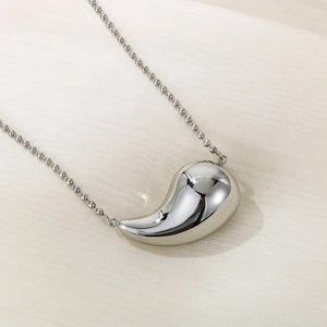Détail du collier argenté avec pendentif goutte d'eau sur tissu texturé beige clair