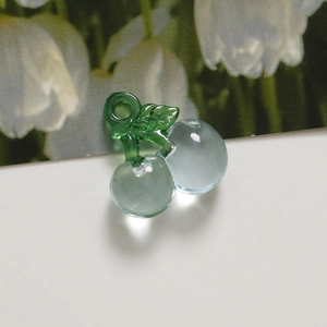 Macro detail of transparent blue cherry resin charms with green leaves and hanging holes